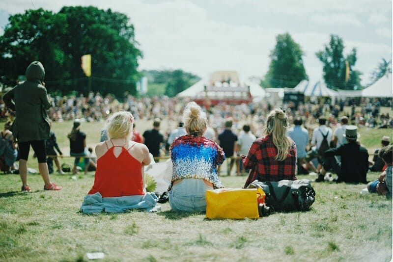 Photo of girls sitting on the grass attending a music festival