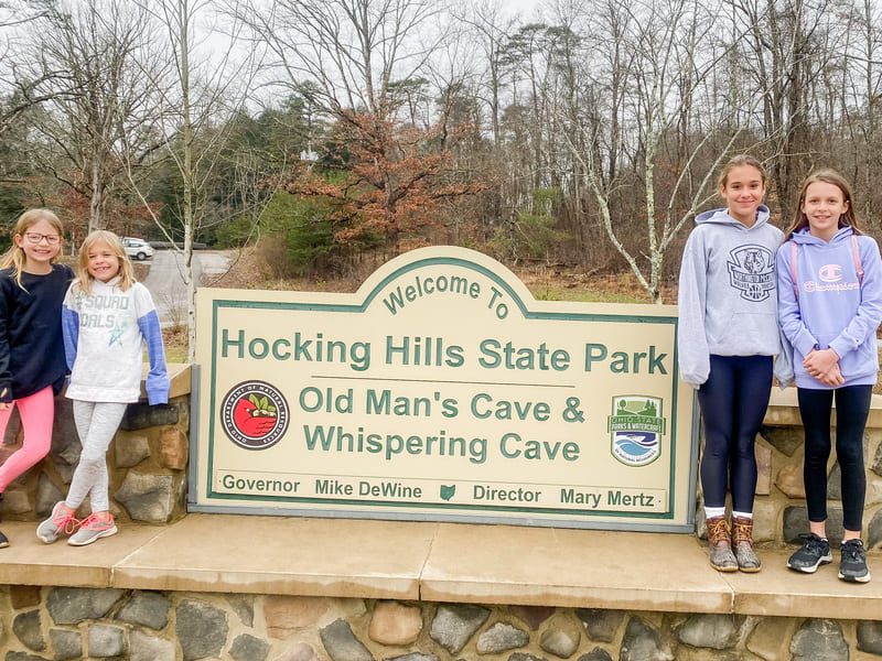A photo of kids by the sign of Hocking Hills State Park's Old Man's Cave and Whispering Cave.